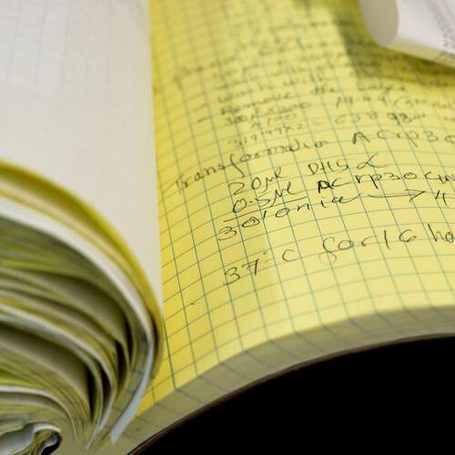 A chemistry lab notebook stuffed with papers, open to a page of yellow graph paper with notes